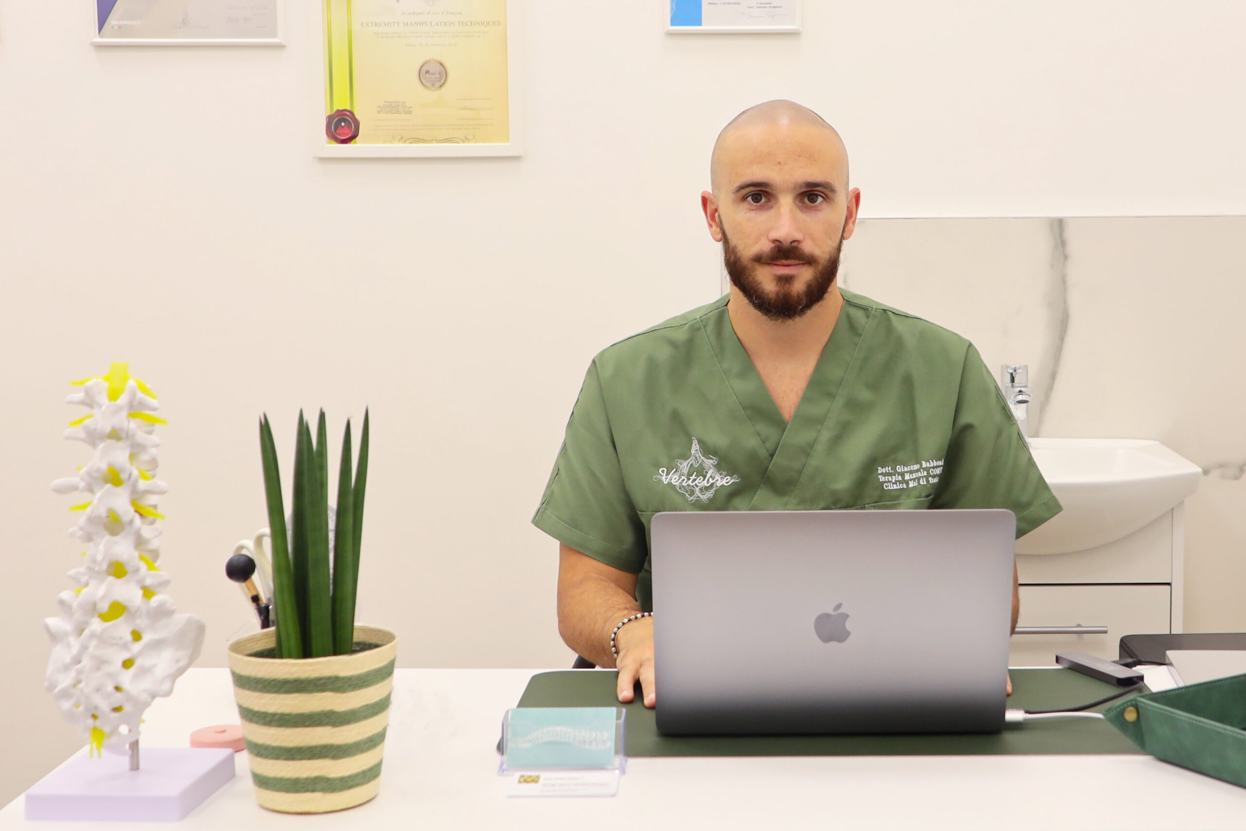 Medico seduto alla scrivania con modello anatomico di colonna vertebrale e computer
